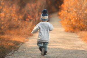 Little boy running on the road past autumn leaves